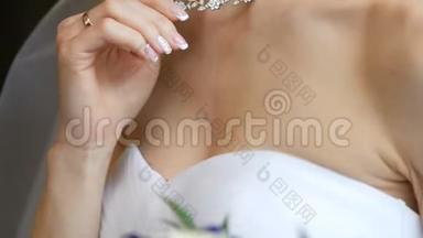 新娘用精致的手拿着项链，项链在脖子上。 新娘结婚的早晨。 广告珠宝。